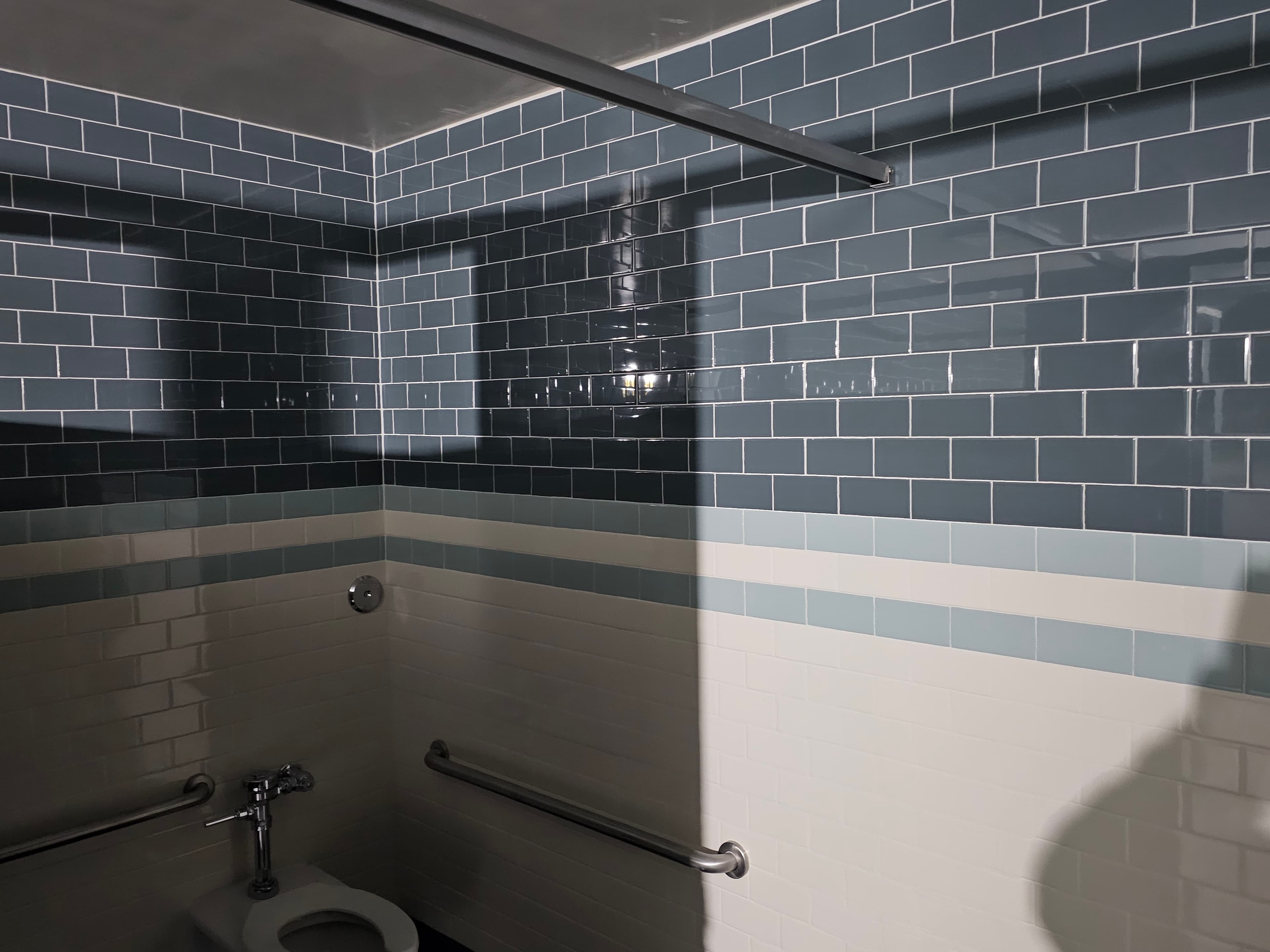 Irvine commercial restroom interior with blue subway walls, banded accent stripe, and ADA grab-bar shower fixtures