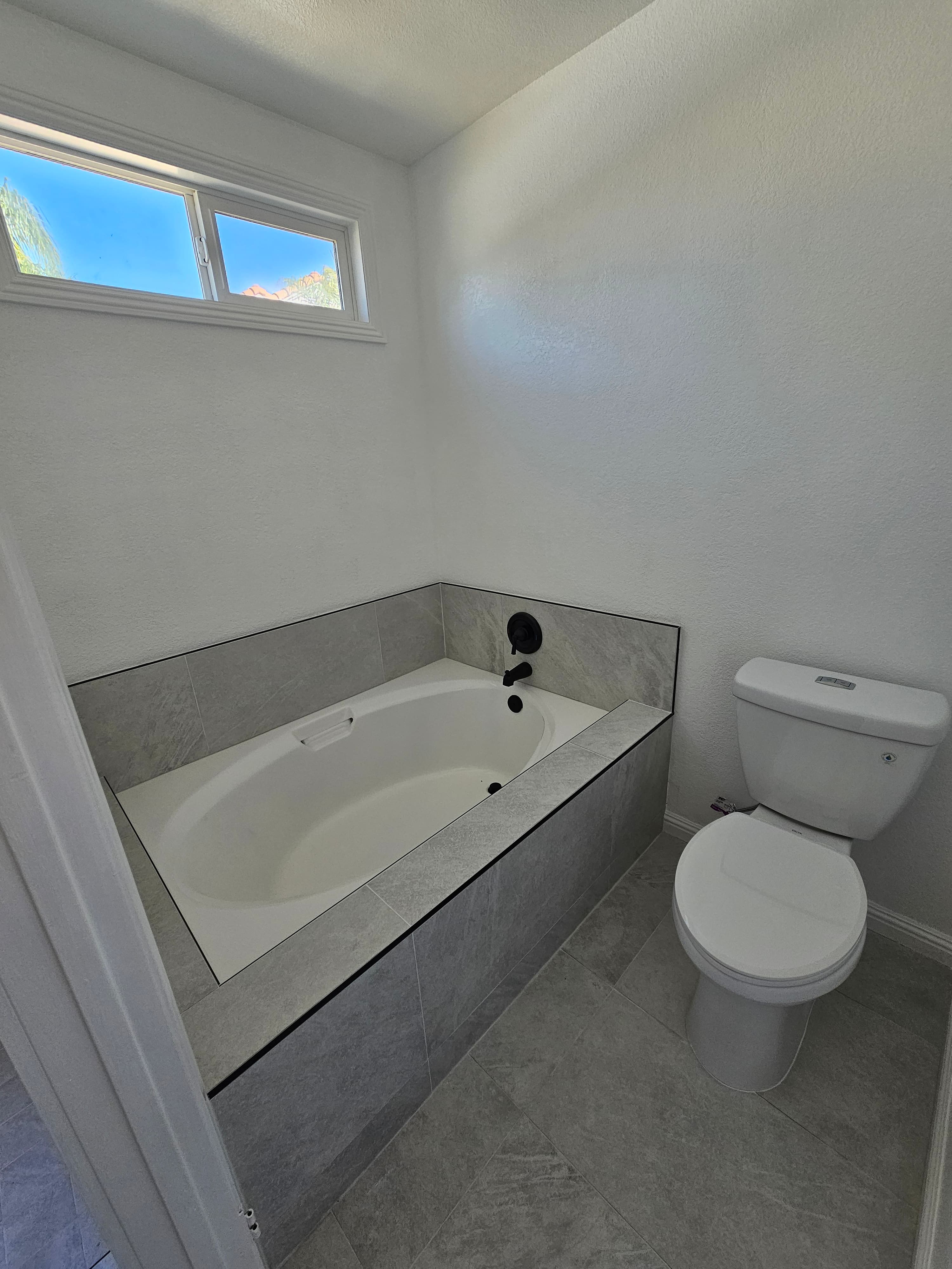 Finished Murrieta bathroom with gray tile surround, marble shower bench, and dual vanity