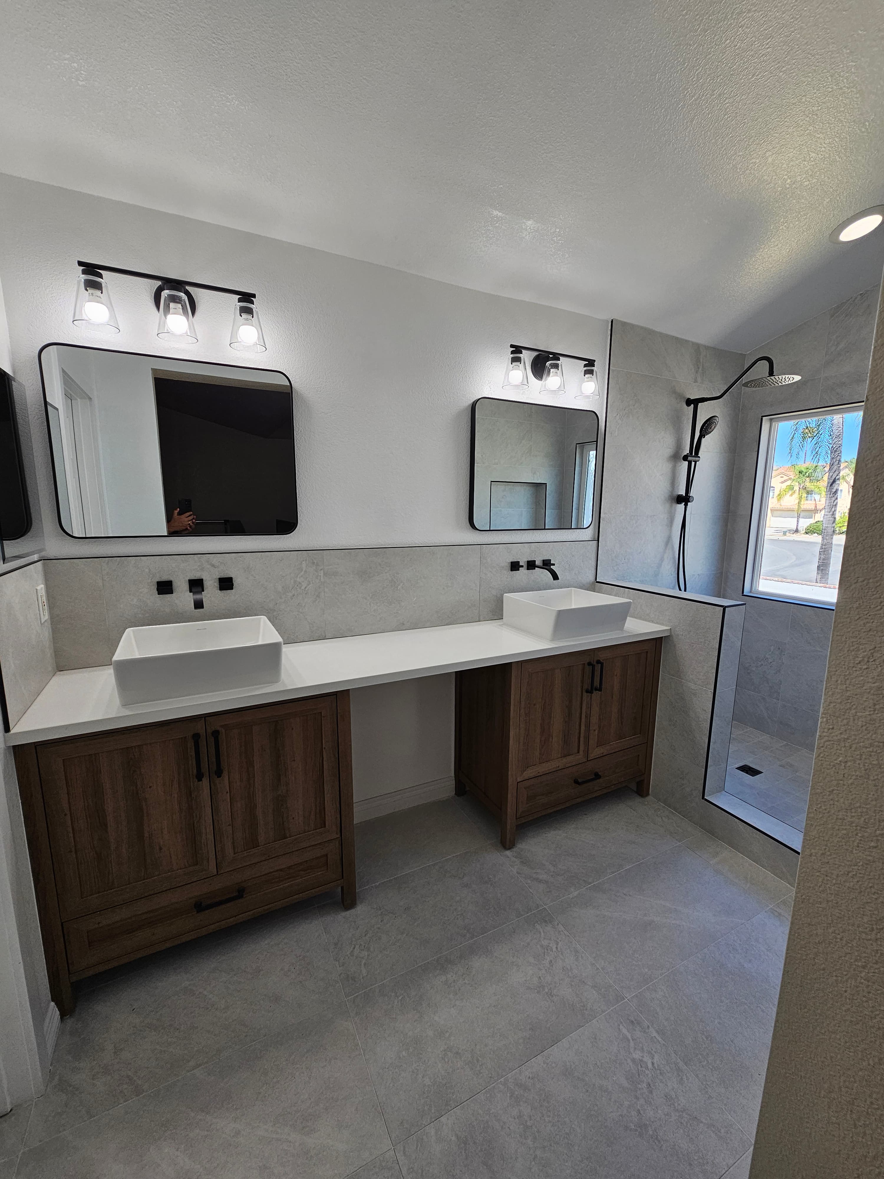 Renovated Murrieta primary bath with double vessel-sink vanity, dark wood cabinetry, large-format porcelain walls, and walk-in marble shower