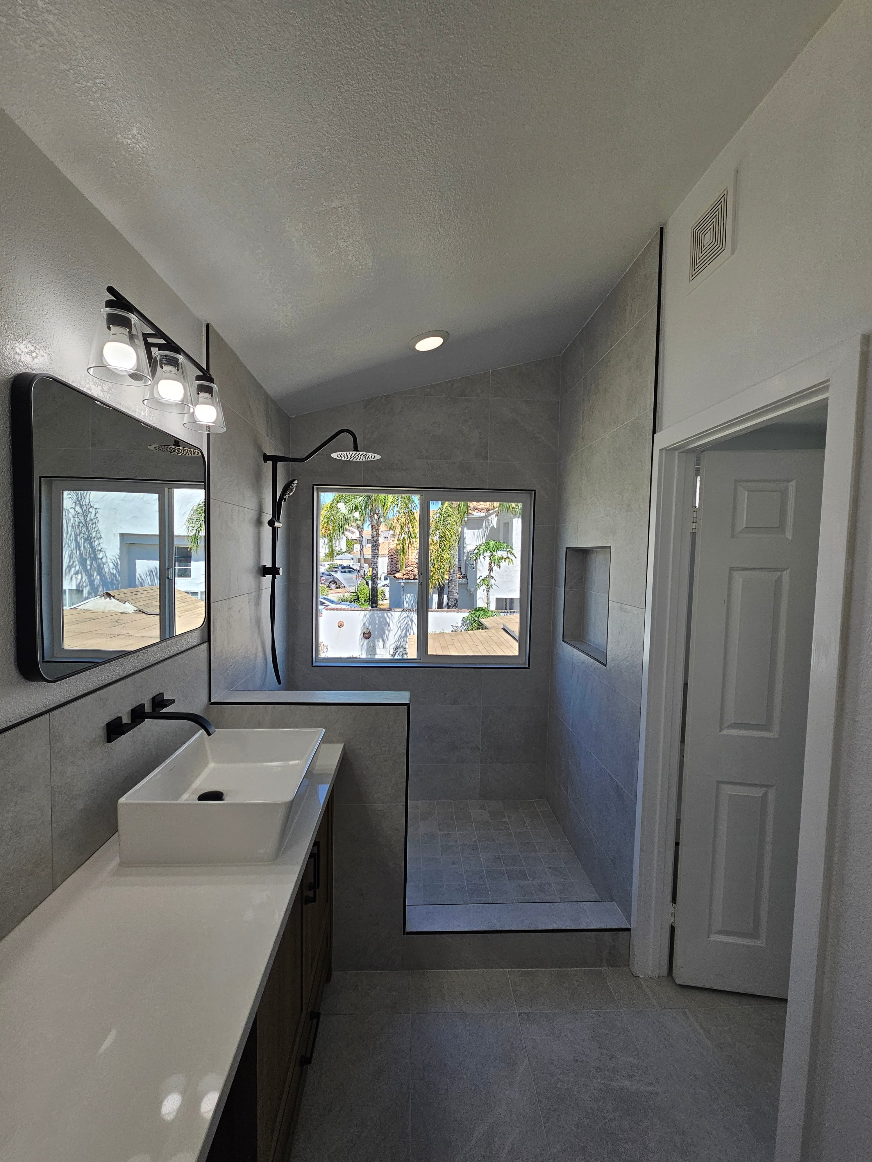 Renovated Murrieta primary bath looking down the galley toward a walk-in porcelain shower with built-in niche and window flooding the space with light