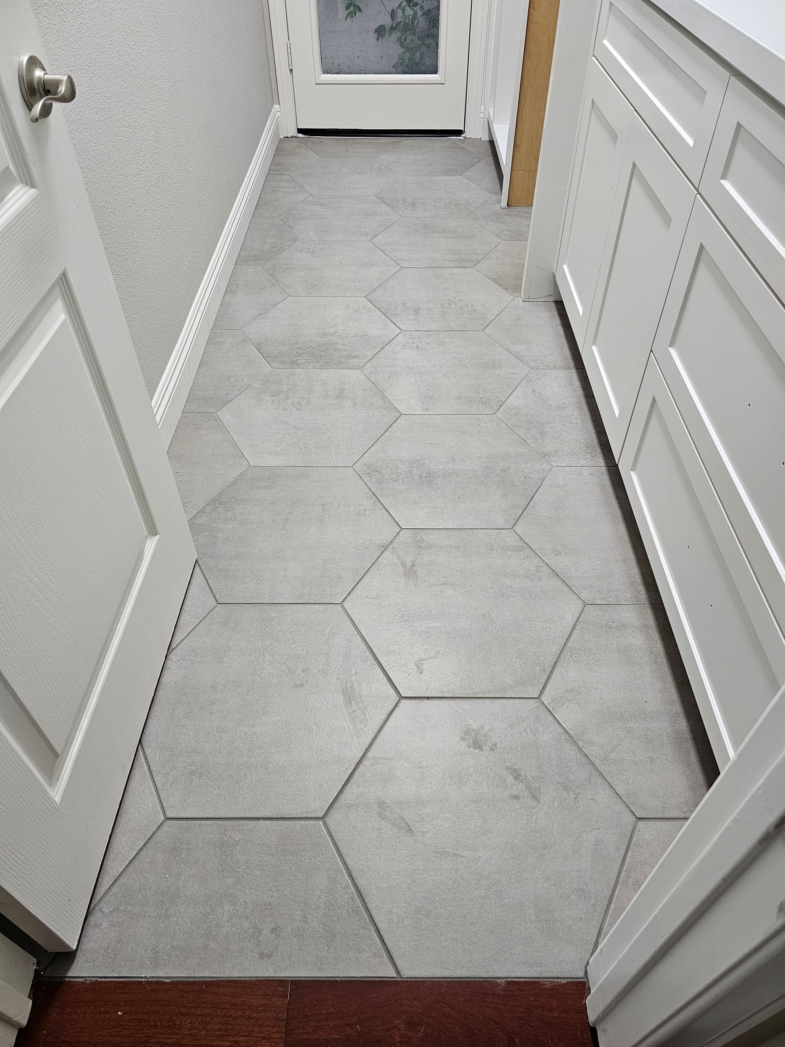 Santa Margarita butler's pantry with large-format hexagon stone flooring running between white shaker cabinetry toward an exterior glass door